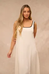 Vestido largo color crudo, sin mangas, con escote redondo y finos ribetes negros en el cuello y las sisas.