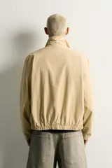 Cazadora regular fit de color beige, confeccionada en mezcla de algodón y lyocell. Cuenta con cuello camisero, cierre frontal de cremallera, bolsillos de plastrón en la cadera, mangas largas con puños elásticos y bajo con ajuste elástico.