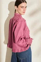 Camisa de lino color morado, con cuello mao, cierre frontal con botones y mangas largas con puños estructurados. Presenta detalles de volados frontales y ruedo con terminaciones desflecadas.