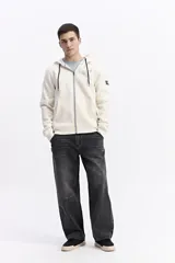 Campera con capucha y cierre frontal, color crema, con bolsillo canguro. Presenta un estampado de texto en el pecho y detalles en el puño.