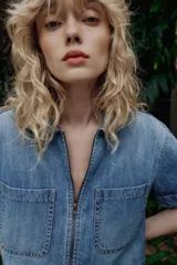 Camisa de denim de corte recto y manga corta, con cuello solapa, cierre frontal con cremallera y dos bolsillos delanteros de plastrón.