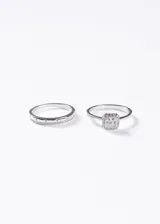 Set de dos anillos de plata 925, uno con diseño de medio sin fin con incrustaciones de zirconias y otro modelo cintillo con zirconia central de corte cuadrado rodeada de piedras pequeñas.