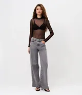 Pantalón de jean color gris lavado, con corte wide leg de piernas amplias y cintura baja. Presenta detalle de tachas metálicas a lo largo de las costuras laterales, cierre frontal con botón y bolsillos funcionales.