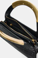 Bolso de mano negro con textura de cocodrilo en relieve, doble asa metálica dorada y cadena bandolera extraíble. Cuenta con cierre de cremallera y bolsillo interior con cremallera.