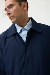 Gabardina azul marino con cuello clásico, cierre frontal con botones y bolsillos laterales.
