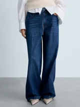 Pantalón de jean estilo wide leg, de tiro medio y color azul oscuro. Cuenta con cierre frontal de cremallera y botón, cinco bolsillos y trabillas para cinturón.