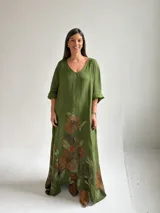 Vestido largo de lino color verde pistacho, con escote en V, mangas tres cuartos y amplio diseño holgado. Presenta un estampado floral grande y artístico en la parte inferior de la falda.