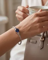 Pulsera de plata con diseño trenzado y una piedra circonia redonda facetada en color azul zafiro en el centro.