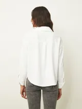 Blusa de color blanco con cuello en V y mangas largas con puños abotonados. Presenta un diseño de corte recto y holgado.