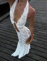 Vestido largo de encaje blanco con diseño semitransparente, escote halter profundo, recortes en la cintura y silueta al cuerpo.