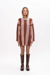 Buzo tipo poncho de corte oversize, con diseño de bloques verticales en tonos marrón y rosado. Presenta cuello redondo en color celeste, mangas largas y bolsillos laterales integrados.