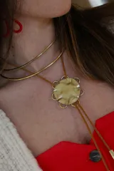 Corbatín con dije de bronce con forma de flor y tiras de cuero sintético marrón con detalles metálicos dorados.