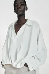 Camisa de cuello solapa y escote en pico, manga larga con puños y detalle de pliegues en el delantero. Presenta un diseño de bajo asimétrico.