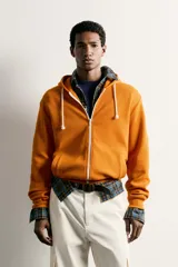Sudadera con capucha y cierre frontal de cremallera, de corte relaxed fit, confeccionada en tejido de algodón con estructura waffle en color naranja. Cuenta con bolsillos frontales de vivo, cordones ajustables blancos y acabados en rib.