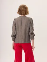 Camisa de algodón color marrón oscuro, con cuello mao, cierre frontal con botones y detalle de volados en la tapeta. Presenta mangas largas con puños elásticos y diseño fluido.