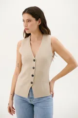 Chaleco tejido de punto en color beige, con escote en V, cierre frontal con botones oscuros y bolsillos frontales decorativos.