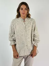 Camisa beige con bordado calado, cuello con volados y mangas largas con puños elásticos.