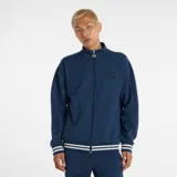 Campera deportiva New Balance, color azul marino, con cierre frontal y cuello alto. Presenta puños y cintura con ribetes a rayas blancas y azul marino. Tiene un pequeño logo bordado en el pecho izquierdo y un tirador de cierre con el logo NB.