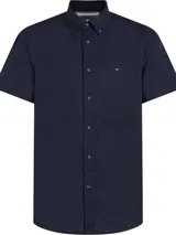 Camisa de manga corta Tommy Hilfiger confeccionada en popelín de algodón, con cuello abotonado y cierre frontal de botones. Presenta un corte regular y el logo de la marca bordado en el pecho.
