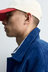 Cazadora estilo varsity confeccionada en pana de algodón azul, con interior ligeramente acolchado. Presenta cuello solapa, cierre frontal con botones a presión, bolsillos laterales de vivo y acabados en rib a rayas en puños y cintura. Incluye múltiples parches bordados decorativos en el frente.