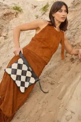 Cartera tipo sobre con diseño de ajedrez en rombos de cuero blanco y negro. Cuenta con una correa de mano integrada y detalle de placa metálica con logo.