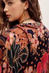 Vestido midi de viscosa con estampado floral en tonos rojos, naranjas y negros sobre base oscura. Cuenta con mangas cortas amplias, escote en V con cuello tipo camisero y cierre frontal de botones.