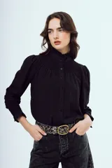 Camisa negra de manga larga con cuello alto gorguera y detalles fruncidos con nido de abeja en el pecho y los puños. Cierre frontal con botones.