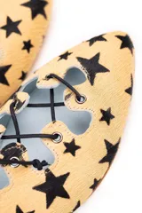 Semibotín de piel de pony con estampado de estrellas negras sobre fondo ocre. Presenta un diseño con abertura escotada, cierre de cordones negros a contraste y punta afilada. Incluye cuña interna y suela de cuero.