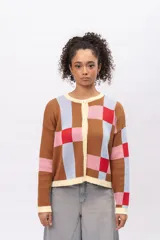 Saco tipo cardigan de tejido de punto con diseño geométrico de cuadros en tonos marrón, celeste, rosa y rojo. Presenta cuello redondo, cierre frontal con botones y terminaciones en color crema.