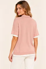 Remera polo de punto color rosa viejo, de manga corta con puños acanalados, cuello camisero y cartera con tres botones. Cuenta con un diseño superpuesto que deja ver una prenda interior blanca en el cuello, mangas y ruedo.