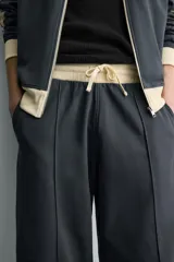 Pantalón jogger de corte wide fit en tejido compacto color gris oscuro. Presenta cintura elástica con cordón ajustable, bandas laterales en contraste color beige y costuras frontales tipo pinza.