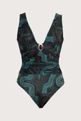 Traje de baño enterizo con escote en V profundo y detalle de aplique metálico con piedra en el centro. Presenta un diseño drapeado en la cintura y un estampado geométrico de ondas en tonos oscuros y turquesa.