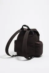 Mochila de nylon color marrón oscuro, con estructura blanda, cierre principal mediante cordón y solapa superior asegurada con hebilla de plástico gris. Posee dos bolsillos frontales con fuelle y asas ajustables.