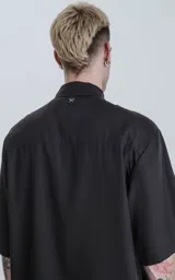 Camisa de manga corta color negro, con cuello clásico y cierre frontal de botones.