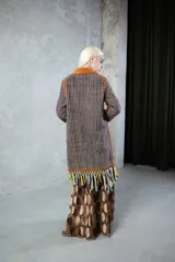 Tapado artesanal de lana con diseño de tejido de red en tonos marrones y negros. Presenta apliques de cuero natural en los bordes y una terminación de flecos largos en el ruedo.