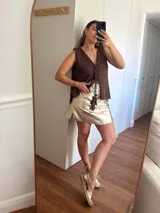 Chaleco tejido en punto calado con hilo de algodón y lurex, de color negro con destellos plateados. Presenta escote profundo en V, cierre frontal con cordones entrelazados terminados en borlas y un corte recto y holgado.