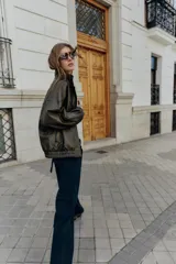 Cazadora estilo bomber color marrón oscuro, con efecto piel, cuello subido y manga larga. Tiene bolsillos delanteros con cierre de cremallera y acabados elásticos en puños y bajo. El cierre frontal es con cremallera y botones a presión ocultos.