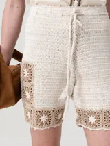 Short tejido a crochet de color beige con detalles geométricos en tono marrón en el borde inferior y lateral. Cuenta con cintura elástica y cordón ajustable con borlas.