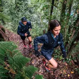 Campera cortaviento con capucha, estampado camuflado en tonos grises y logo Merrell en el pecho. Cierre frontal con cremallera y bolsillos laterales. Ideal para trail running.