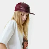 Gorra tipo trucker bordó, con frente de cuero sintético y paneles traseros de malla. Cuenta con visera plana y diseño con escudo bordado en la parte frontal.