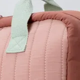 Mochila acolchada con diseño capitoné en tonos rosados y beige, con asas de mano color verde menta. Presenta un bolsillo frontal con un dije de flor sonriente.