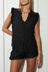 Blusa negra sin mangas confeccionada en gasa plisada, con detalle de volados en los hombros y botones de nácar en la parte delantera.