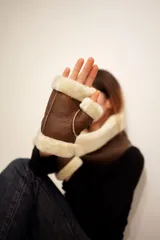 Mitones sin dedos confeccionados en cuero napalan color habano, con forro interior de lana natural en tono crema y bordes expuestos del mismo material.