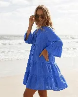 Vestido corto de lino color azul, de corte amplio y silueta en capas con volados, mangas tres cuartos acampanadas y cierre frontal con botones.