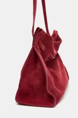 Bolso de hombro confeccionado en serraje color bordó, con diseño de tira entrelazada en la parte frontal, asa larga y cierre mediante botón imantado.
