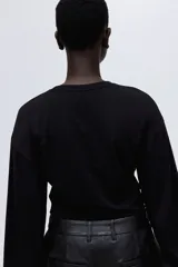 Top de manga larga en tejido de punto suave, con cuello redondo, hombros caídos y mangas acampanadas. Presenta un diseño con bajo recto y aberturas laterales.