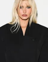 Blazer negro de corte oversize con hombros estructurados, diseño cruzado asimétrico y cierre frontal con un botón. Prenda forrada de manga larga.