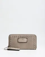 Billetera grande tipo fichero de cuero sintético color taupe, con cierre perimetral, detalles de tachas metálicas plateadas en los bordes y placa frontal con la inscripción de la marca Extra Large. Incluye una tira de mano desmontable con argolla metálica.