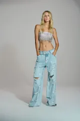 Jean wide leg de mujer en denim azul claro, con efecto desgastado, aberturas y aplicaciones de pedrería brillante distribuidas a lo largo de la silueta.
