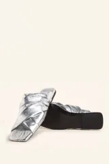 Sandalia tipo slide de cuero vacuno color blanco, con diseño de tiras cruzadas y fruncidas. Presenta una puntera cuadrada y una suela plana de cuero con un pequeño taco de 2 cm.